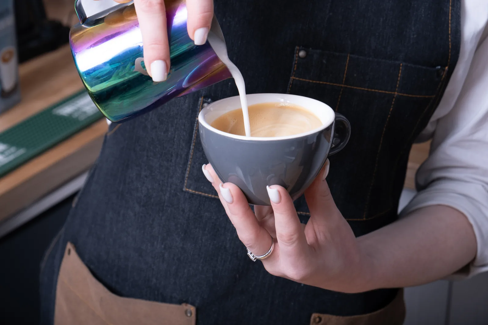 Barista versant un trait de lait texturé dans un cappuccino dans un coffee shop belge en 2026.