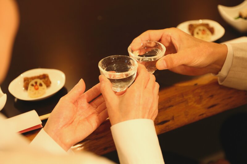 Deux mains trinquent avec de petites coupes de saké au Restaurant Kamo, Bruxelles